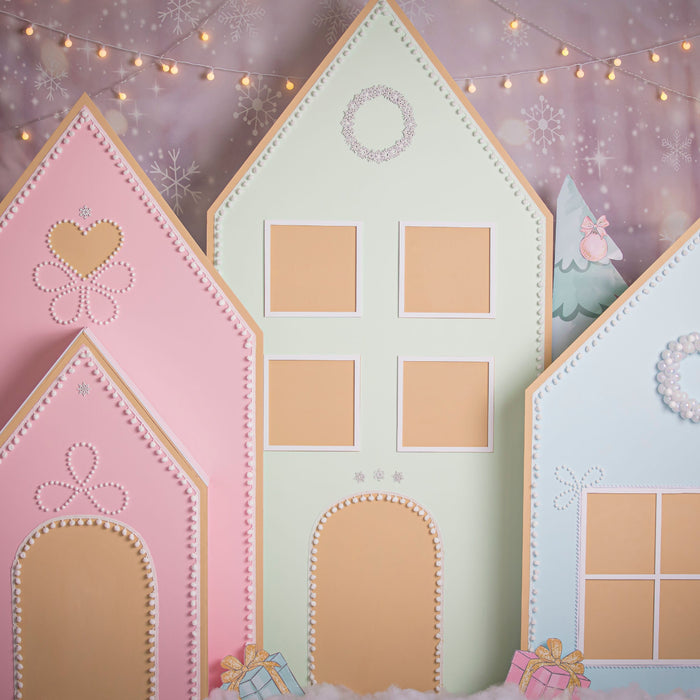 Pastel gingerbread village backdrop featuring three oversized foam board houses in pink, mint green, and light blue, decorated with candy-inspired details, faux snow, and twinkle lights—perfect for Christmas parties, photo sessions, or festive holiday decor.