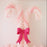 Two oversized candy cane columns made entirely of pastel pink and white balloons stand side by side, styled with a smooth gradient effect from light to darker pink. A large hot pink paper bow is placed at the center where the two balloon candy canes cross, creating a cute holiday focal point perfect for Christmas parties, photo ops, and festive backdrops.