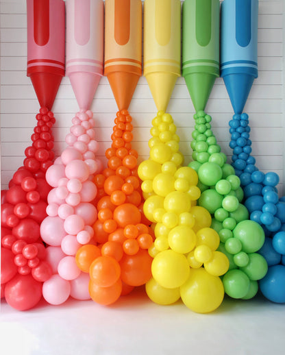 Oversized rainbow crayon props with matching balloon garlands spilling from each crayon tip, creating a vibrant, colorful classroom or party backdrop. Designed by Lilly Jimenez for her Crayon Prop Tutorial at Creative Heart Studio, this display is perfect for back-to-school events, photo ops, teacher appreciation setups, or any celebration needing a pop of playful creativity.