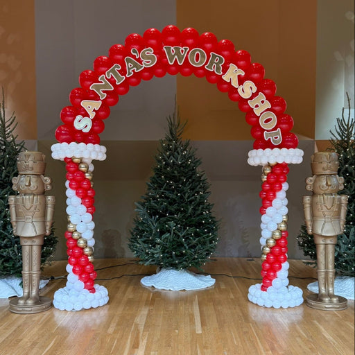 Red and white Santa’s Workshop balloon arch with candy cane style columns and festive Christmas decor, perfect for holiday parties, Santa meet and greets, photo backdrops, and winter event balloon installations.