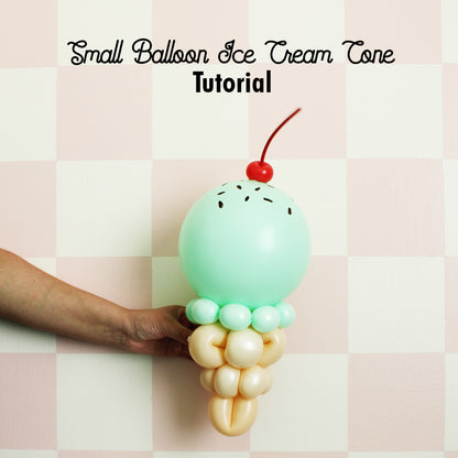 Mint green balloon ice cream cone sculpture with a cherry on top, held by a hand against a pastel pink checkered wall. This adorable small balloon design is perfect for summer-themed parties, dessert tables, or ice cream shop décor. Great for balloon artists and party decorators.