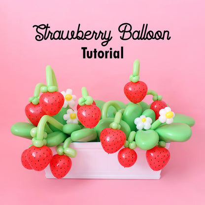 A basket filled with red balloon strawberries and green balloon leaves, accented with white and yellow balloon daisies, styled in front of a pink background. Ideal for strawberry-themed balloon tutorials and summer party decor.
