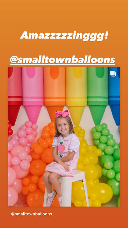 Colorful rainbow balloon backdrop created by @smalltownballoons using Lilly Jimenez’s Crayon Prop Tutorial. Features oversized red, pink, orange, yellow, green, and blue crayon props with coordinating balloon garlands. A young girl sits in front of the display for a vibrant photo op, showcasing how this tutorial is perfect for kids’ parties and back-to-school events. A fun, eye-catching student success story from The Creative Heart Studio.