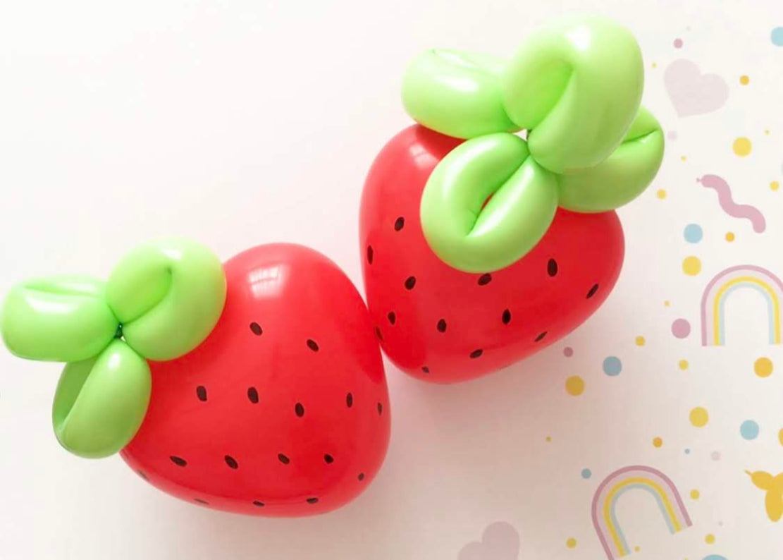Two red balloon strawberries with green twisted balloon tops and hand-drawn black seeds, placed on a white background decorated with pastel rainbows and hearts.