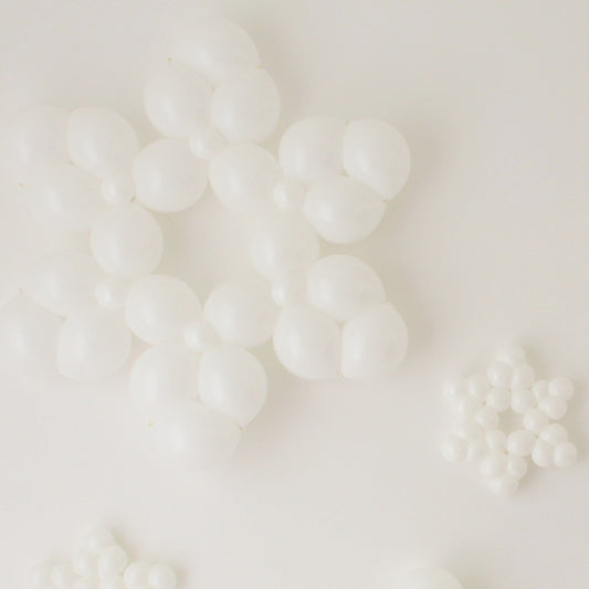 Clustered white balloon snowflakes in multiple sizes lay against a clean white background. Each snowflake is made from small round balloons arranged into layered six-point shapes, creating a bright winter look. The mix of large and small designs adds dimension, making these balloon snowflakes perfect for holiday parties, winter wonderland themes, and seasonal photo backdrops.