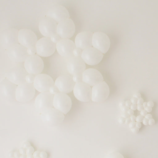 Clustered white balloon snowflakes in multiple sizes lay against a clean white background. Each snowflake is made from small round balloons arranged into layered six-point shapes, creating a bright winter look. The mix of large and small designs adds dimension, making these balloon snowflakes perfect for holiday parties, winter wonderland themes, and seasonal photo backdrops.