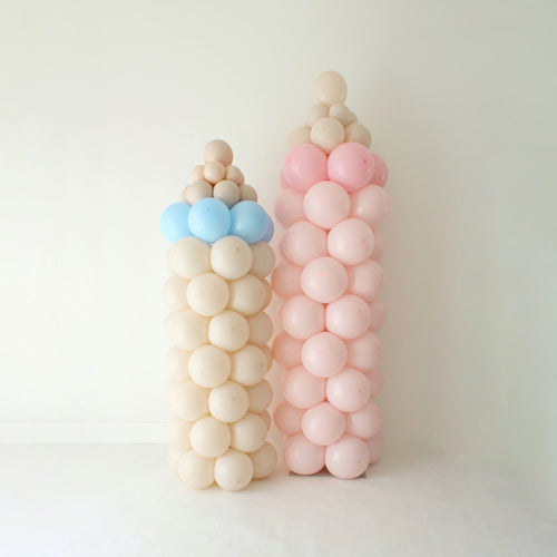 Freestanding baby bottle balloon columns in soft pastel pink, blue, and neutral tones, designed for baby showers, newborn welcome decor, and delivery friendly balloon displays. These stacked balloon columns showcase a clean, modern baby theme and can be paired with a coordinating baby rattle balloon prop for event styling or grab and go orders.