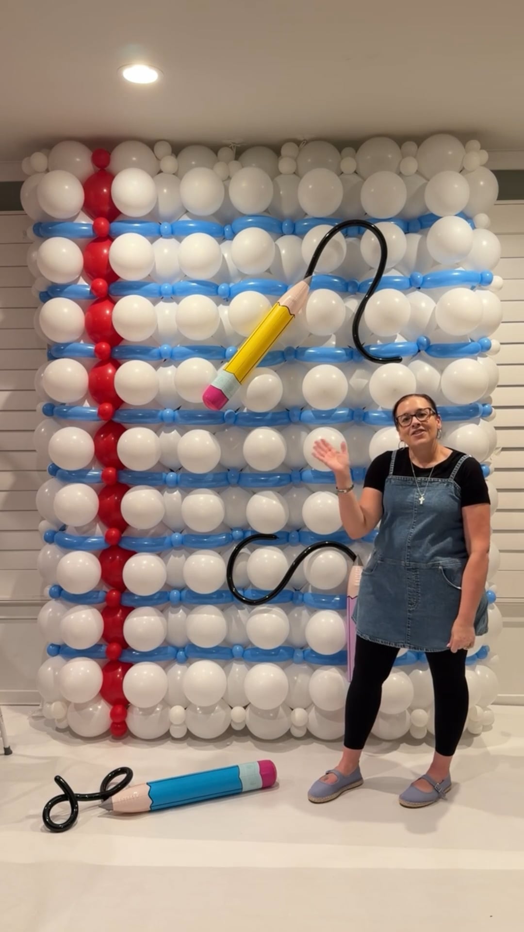Victoria Dzierza standing beside a back-to-school balloon backdrop designed as notebook paper with oversized pencil decorations.