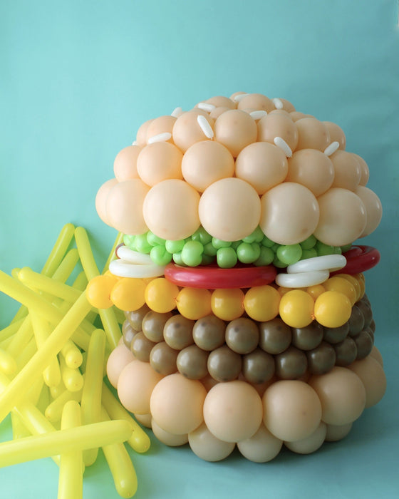 Balloon burger sculpture with yellow balloon fries on blue background