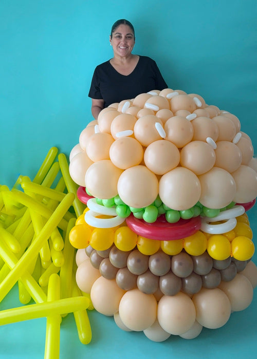 Lilly standing behind large balloon burger sculpture showing scale on blue background