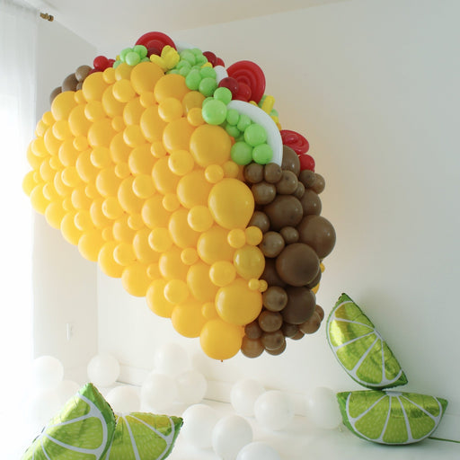 Large balloon taco sculpture with lettuce, tomato, and meat details with lime props on floor