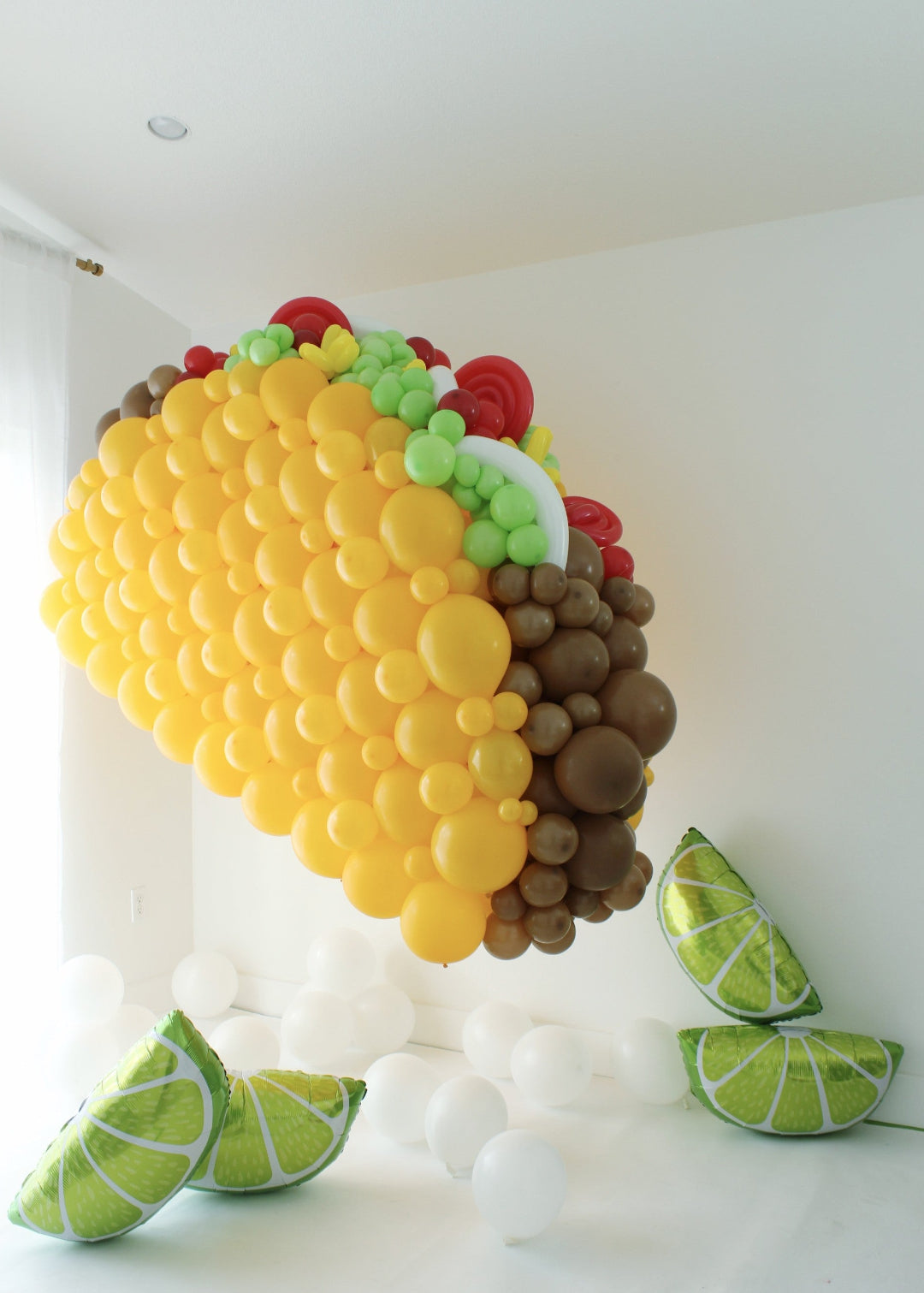 Large balloon taco sculpture with layered fillings and lime slice props on floor
