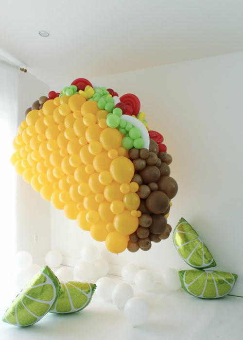 Large balloon taco sculpture with layered fillings and lime slice props on floor