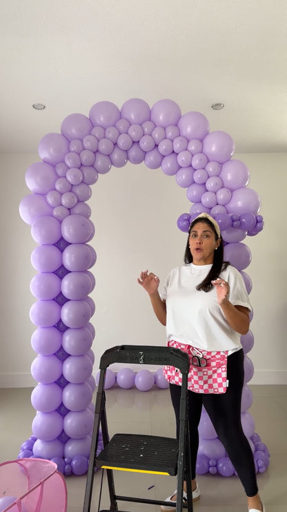 Instructor demonstrating a lavender Candy Yard balloon entrance with tuxedo-style columns and a curved flat-pack arch.