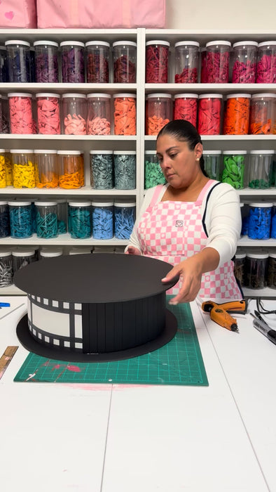 Lilly creating an oversized film reel prop with black foam board and film strip details for a cinema party decor class, movie night decorations, Hollywood themed events, and theater party displays.
