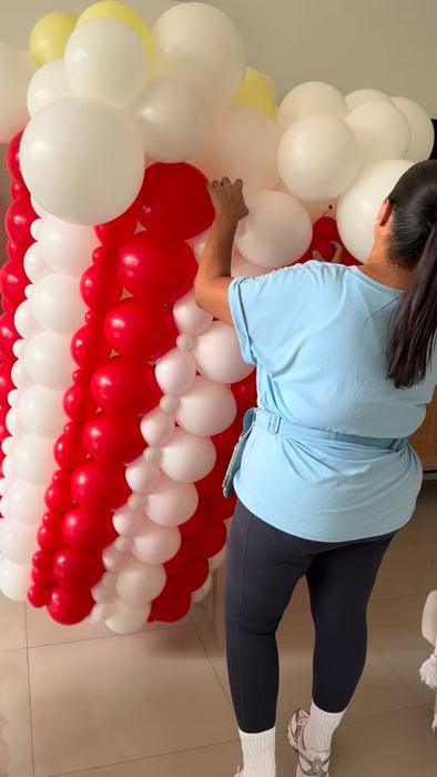 Lilly assembling the giant balloon popcorn bucket with red and white striped balloons, white popcorn balloon clusters, and yellow butter accents for the Cinema Party Decor Class, movie night decorations, and Hollywood themed party displays.