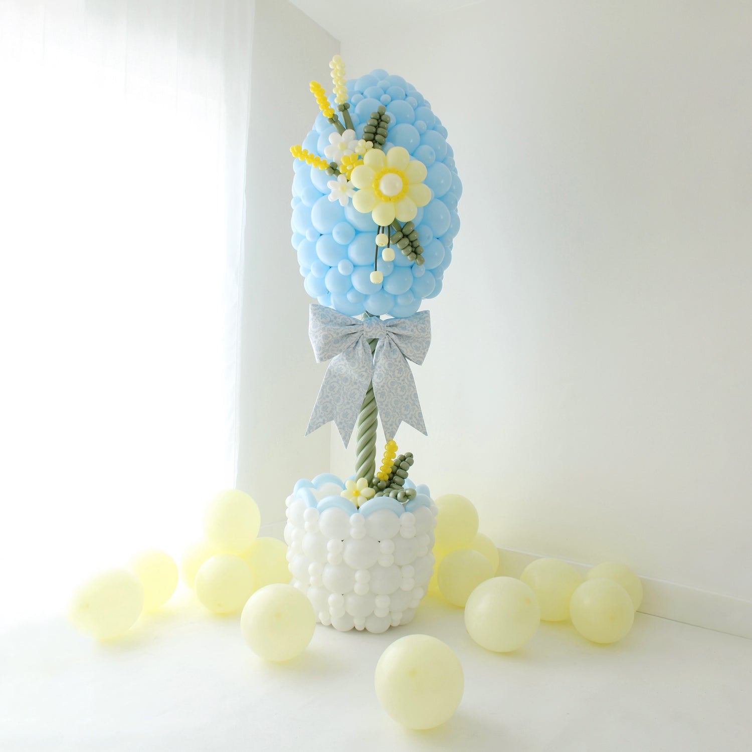 Easter egg balloon column topiary with basket base, balloon flowers, and oversized bow for spring decor and Easter party setup