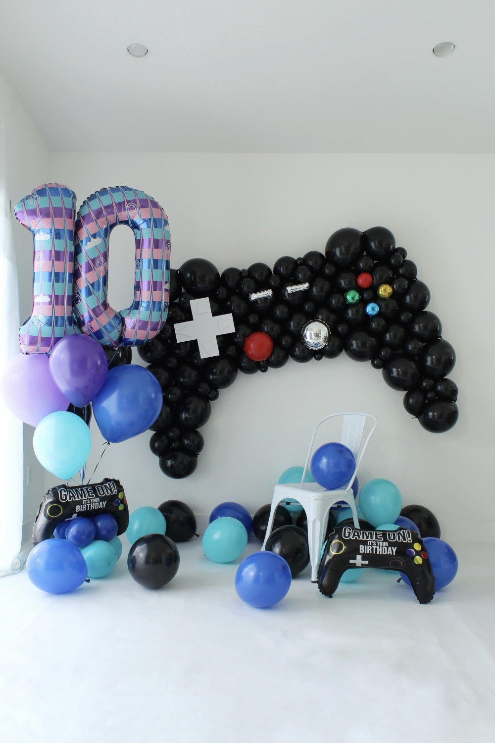Black game controller balloon backdrop beside patterned number 10 balloons, with blue, purple, and aqua balloons and controller foils.