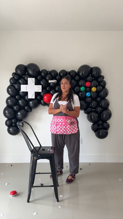 Balloon Instructor, Lilly Jimenez standing in front of an oversized black game controller balloon sculpture with a white directional pad and colorful buttons.