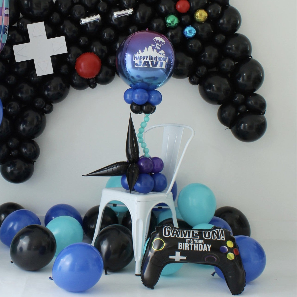 Gamer-themed balloon centerpiece with a personalized ombré orb, blue and purple balloon clusters, and black starburst accents beneath a controller balloon backdrop.