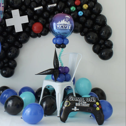 Gamer-themed balloon centerpiece with a personalized ombré orb, blue and purple balloon clusters, and black starburst accents beneath a controller balloon backdrop.