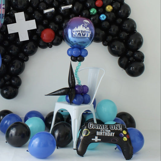 Gamer-themed balloon centerpiece with a personalized ombré orb, blue and purple balloon clusters, and black starburst accents beneath a controller balloon backdrop.