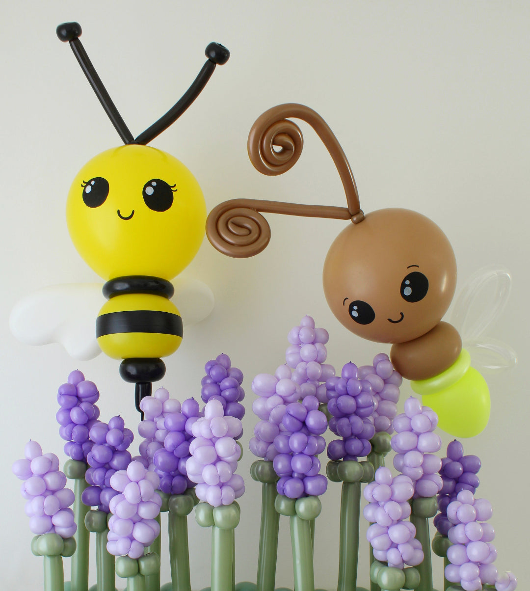 Giant balloon bee and glowing light bug sculpture created by Lilly Jimenez, displayed among purple balloon flowers. Oversized spring balloon decor featuring a yellow and black bee and whimsical light bug, perfect for garden theme parties, birthday backdrops, baby showers and professional balloon installations.