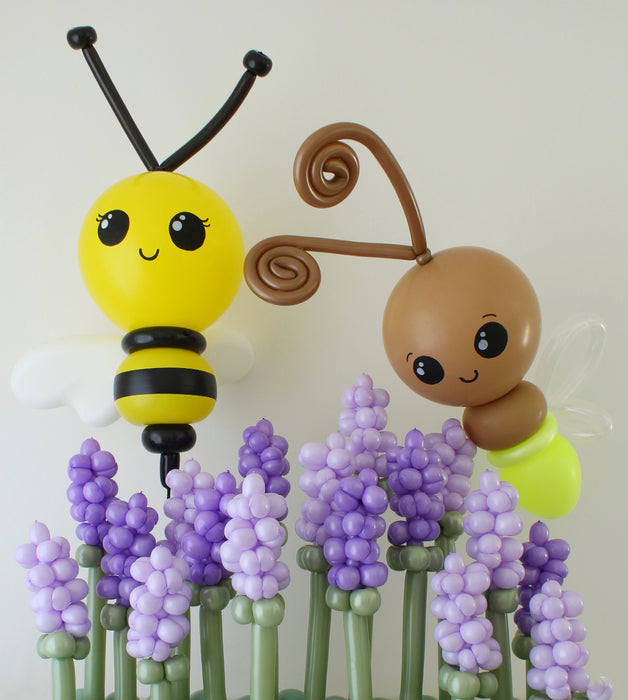 Giant balloon bee and glowing light bug sculpture created by Lilly Jimenez, displayed among purple balloon flowers. Oversized spring balloon decor featuring a yellow and black bee and whimsical light bug, perfect for garden theme parties, birthday backdrops, baby showers and professional balloon installations.