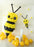 Giant balloon bumble bee sculpture created by Lilly Jimenez featuring layered yellow and black balloon clusters, oversized antennae and white wings. Large scale spring balloon decor displayed with yellow floor balloons and floral wall accents, ideal for garden theme parties, birthdays and professional event backdrops.
