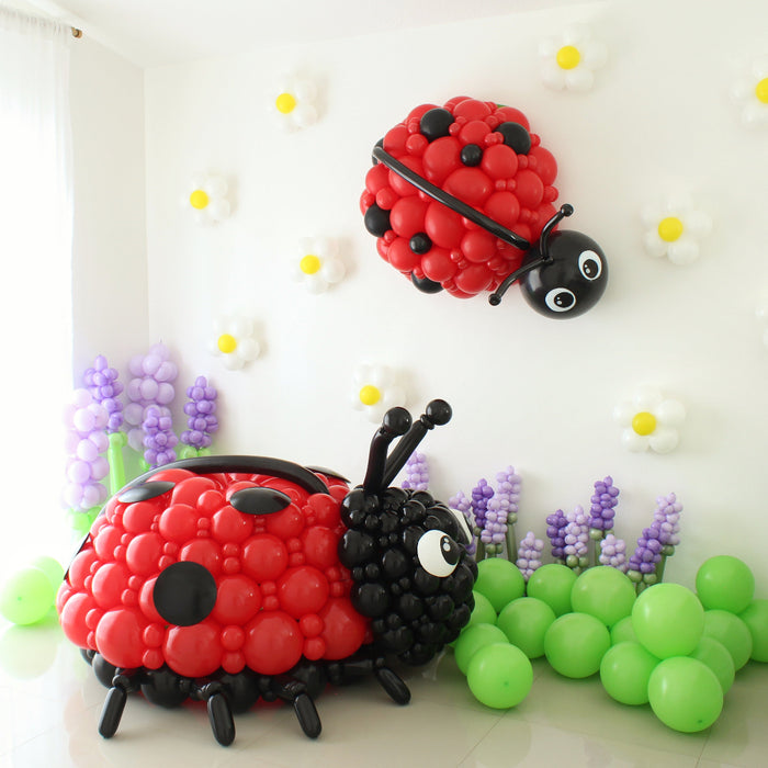 Oversized red and black balloon ladybug sculpture created by Lilly Jimenez for the Giant Balloon Bugs Class. Large balloon decor installation displayed with green balloon clusters and purple floral balloons, perfect for spring parties, garden theme backdrops and birthday event styling.