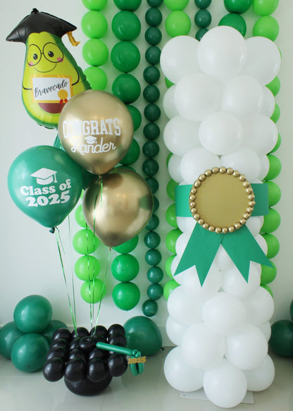 Graduation party setup featuring a white balloon diploma column with a green ribbon, and a matching balloon bouquet anchored by a graduation cap balloon weight. Includes foil and latex balloons with “Class of 2025” and “Congrats Xander” designs, styled in front of a green balloon backdrop.