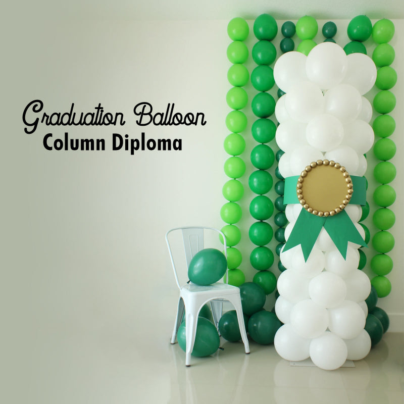 Graduation Balloon Column Diploma made from stacked white balloons with a green ribbon and gold medallion detail, styled in front of a green balloon garland wall. Ideal for photo backdrops or stage decor at graduation parties for any grade level.