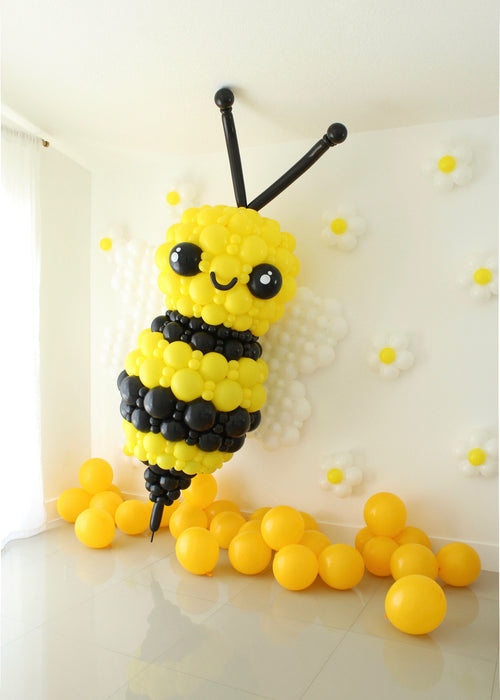 Large scale balloon bumble bee installation featuring clustered yellow and black balloons with extended antennae. Spring themed balloon decor staged with yellow balloons and wall florals, ideal for garden parties, kids birthdays and statement event backdrops.