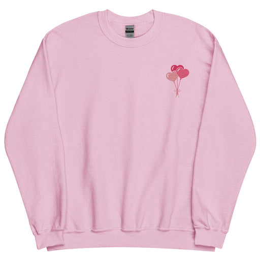 A light pink sweatshirt featuring a minimalist design of three heart-shaped balloons in shades of pink and red, tied together with a small bow, located on the upper left chest area.