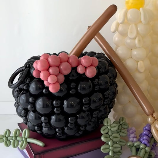 Practical Magic-inspired balloon display featuring a black witch’s cauldron, oversized candles, broom, lavender, and rosemary balloon details.