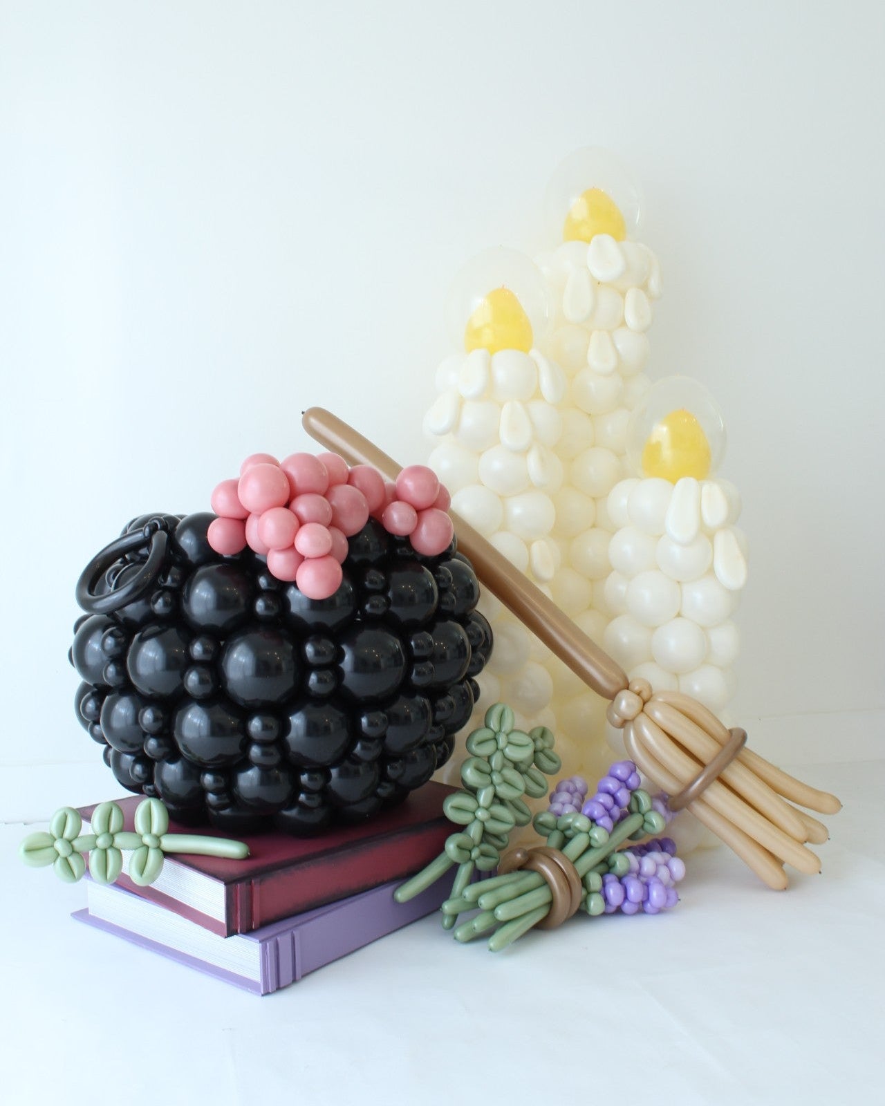Oversized black balloon witch’s cauldron with spoon, balloon candles, broom, lavender, and rosemary in a Halloween-inspired display.