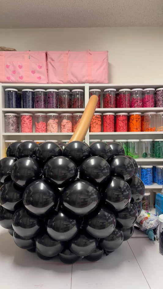 Black balloon witch’s cauldron with oversized spinning balloon spoon during construction at The Creative Heart Studio.