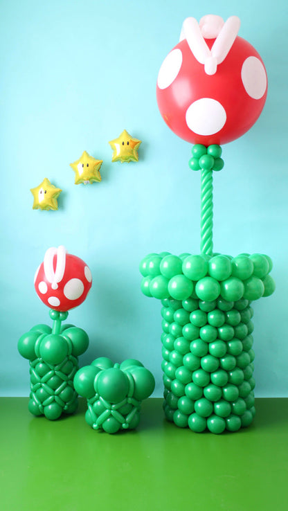 Large and small balloon Piranha Plants in green pipes with star balloons on a blue backdrop.