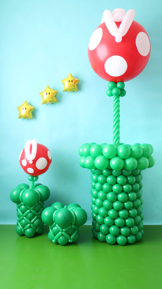 Large and small balloon Piranha Plants in green pipes with star balloons on a blue backdrop.
