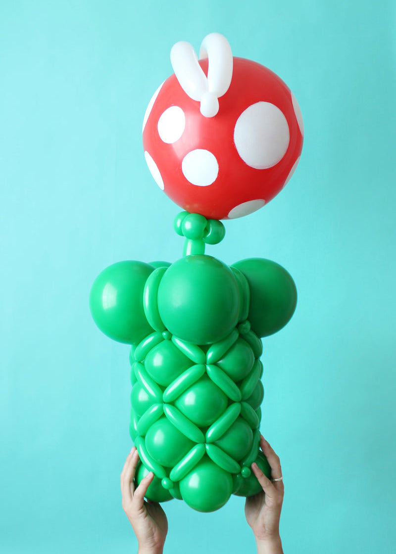 A small balloon Piranha Plant with a green base and red spotted top, held against a blue backdrop.